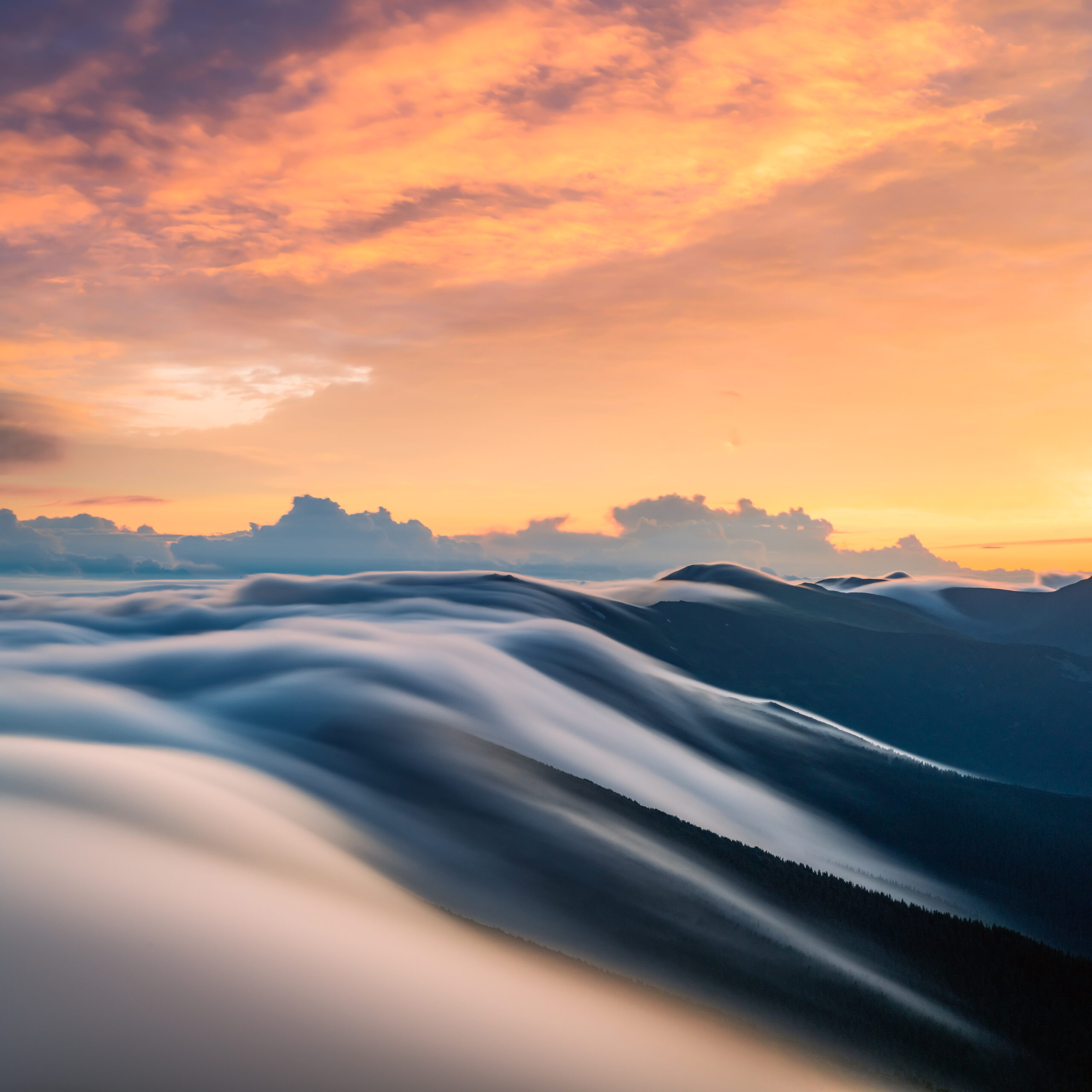 Amazing flowing morning fog in spring mountains blurred from long exposure. Beautiful sunrise on background. Landscape photography